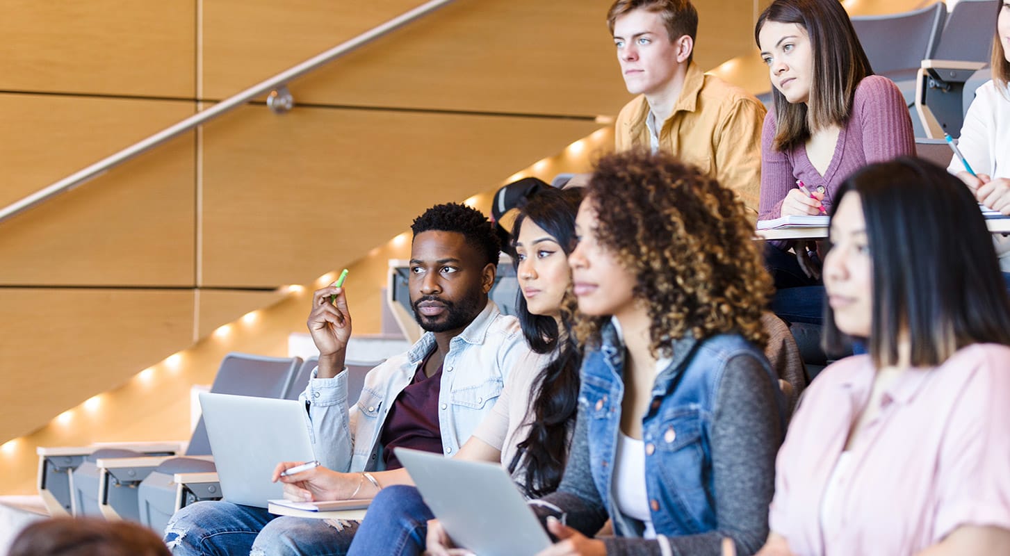 A crowd of students in a lecture hall, arranged in rows, listening to a speaker at the front of the room.